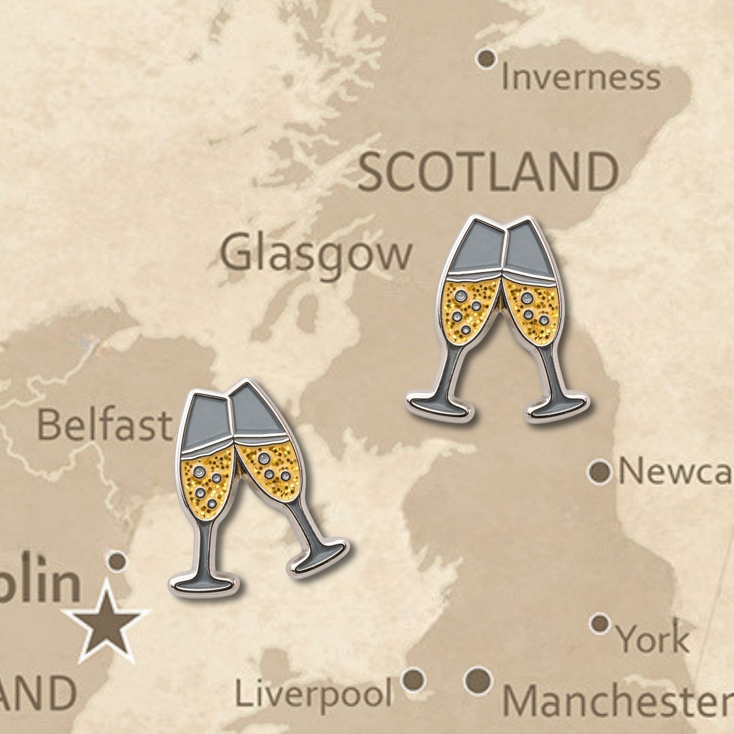 Two champagne flute clinking enamel push pins with gold glitter and nickel outline on vintage map background