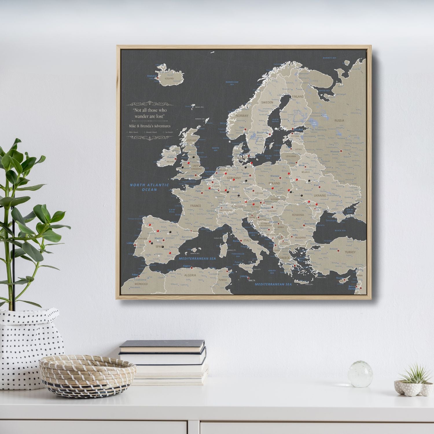 Framed earth toned Europe travel map canvas with red and black pins on white wall