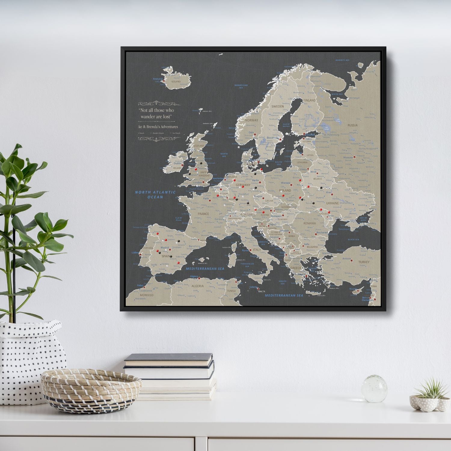 Earth toned Europe travel map canvas with red pins in black float frame hanging on white wall