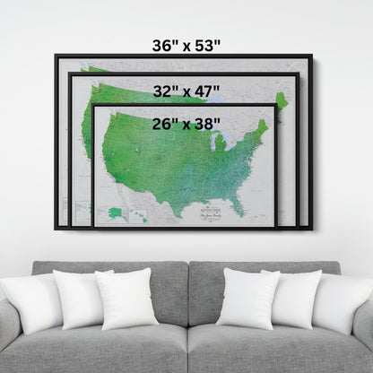 Three black-framed emerald watercolor USA travel map canvases displayed above gray sofa showing size comparison