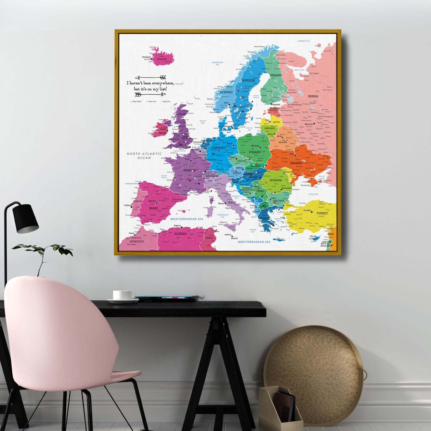 Colorful Europe travel map canvas with gold frame hung above modern desk workspace