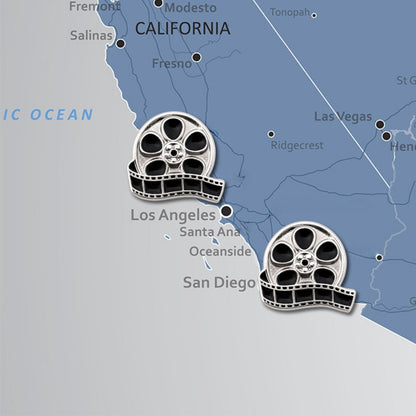 Two silver and black enamel movie reel film push pins displayed on California map near Los Angeles