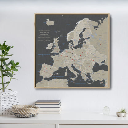 Framed earth toned Europe travel map canvas with red and black pins on white wall